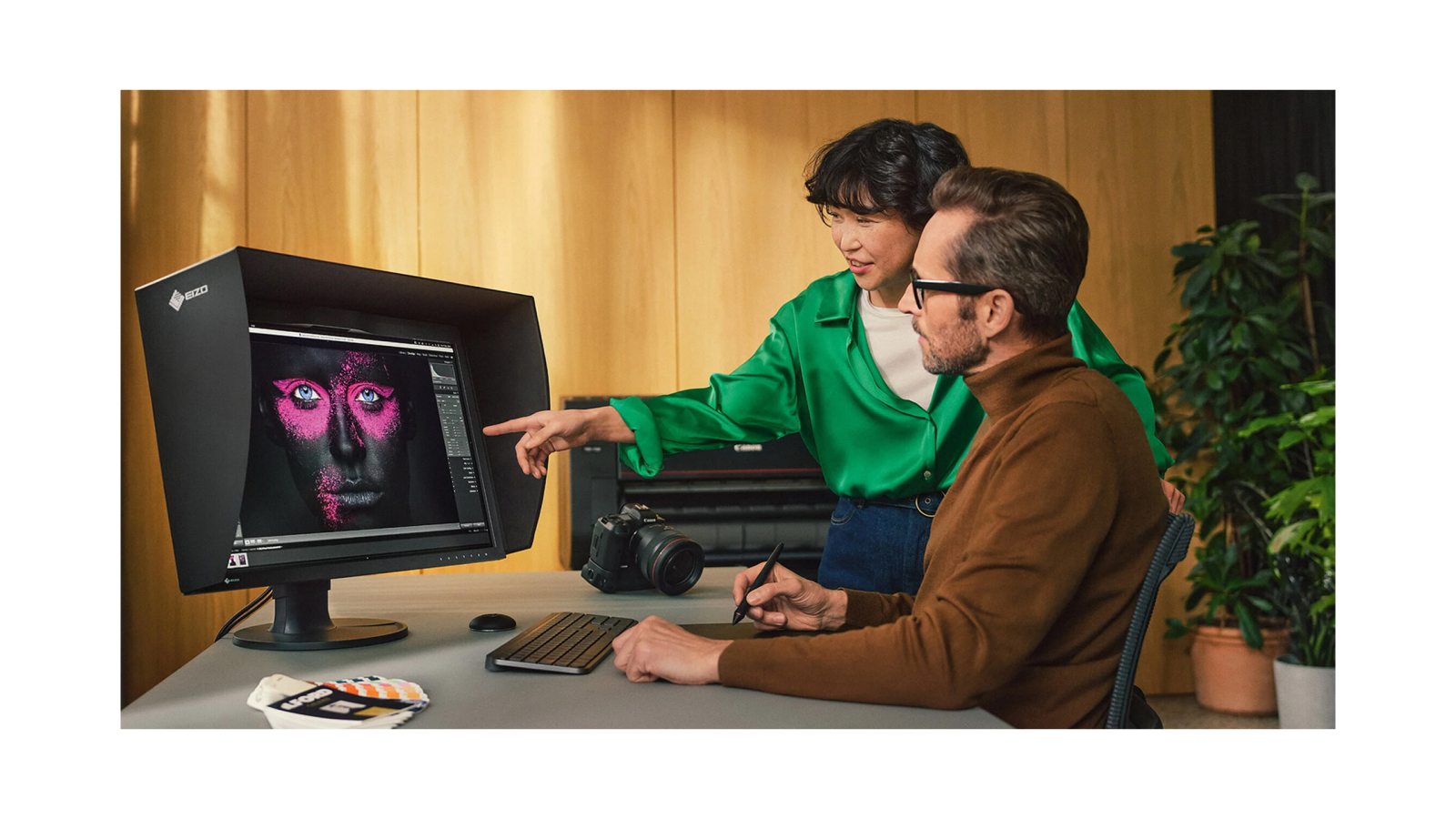 Dos profesionales creativos colaborando frente a un monitor de diseño con visera y tableta gráfica, editando imagen artística.